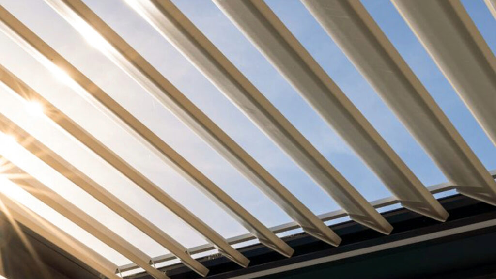Vue en contre-plongée des lames orientables d'une pergola bioclimatique blanche ouverte sous le soleil