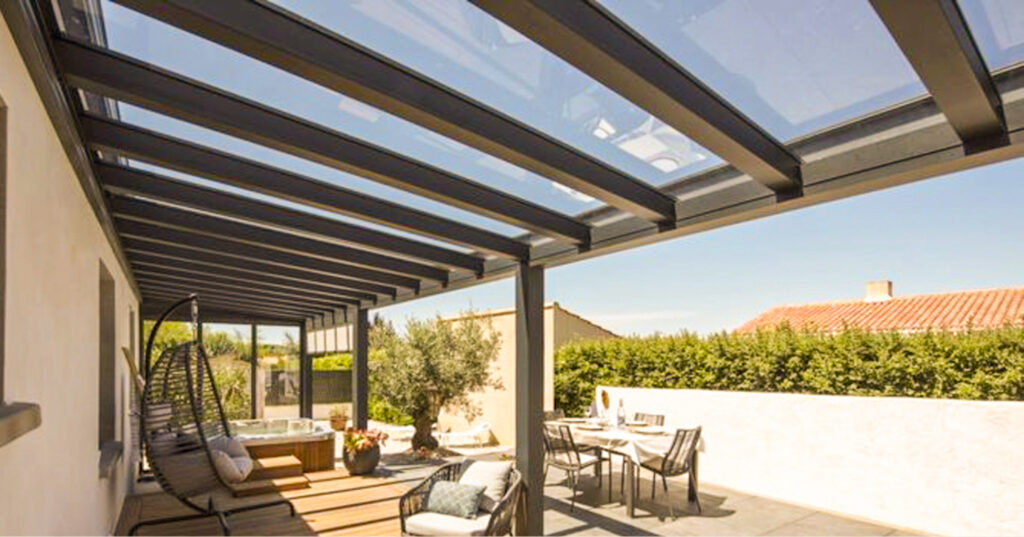 Aménagement extérieur haut de gamme Gustave Rideau : pergola adossée à toiture vitrée créant un véritable espace de vie avec salon de détente et espace repas.